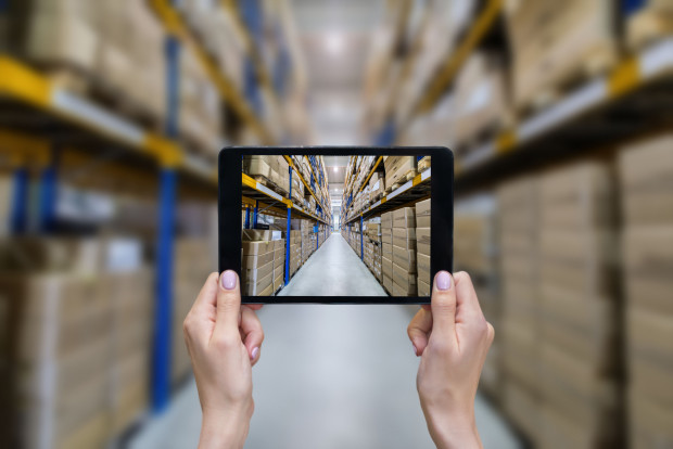 Horizontal color image of female hands holding a digital tablet in a corridor of futuristic distribution warehouse. Ordering online from a modern warehouse on a touchscreen tablet computer. Large distribution storage in background with racks full of packages, boxes, pallets, crates ready to be delivered. Logistics, freight, shipping, receiving.