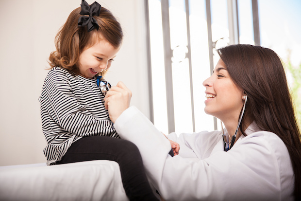 Pretty Hispanic pediatrician examining a little girls' breathing and smiling