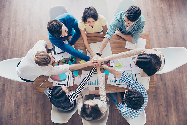 All together! Conception of successful teambuilding. Topview of businesspeople putting their hands on top of each other in nice light workstation, wearing casual clothes